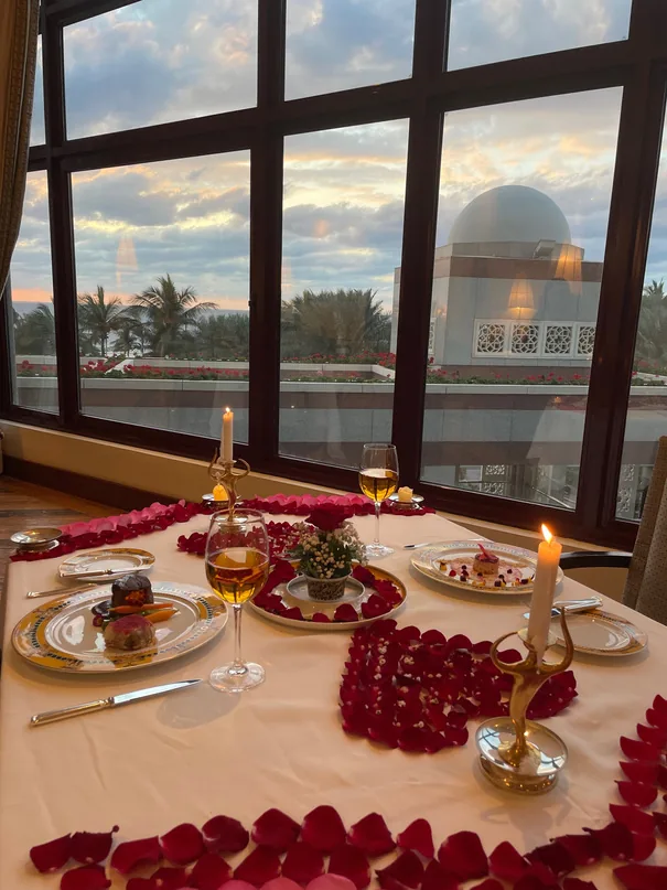 Romantic candlelit dinner table strewn with rose petals at sunset